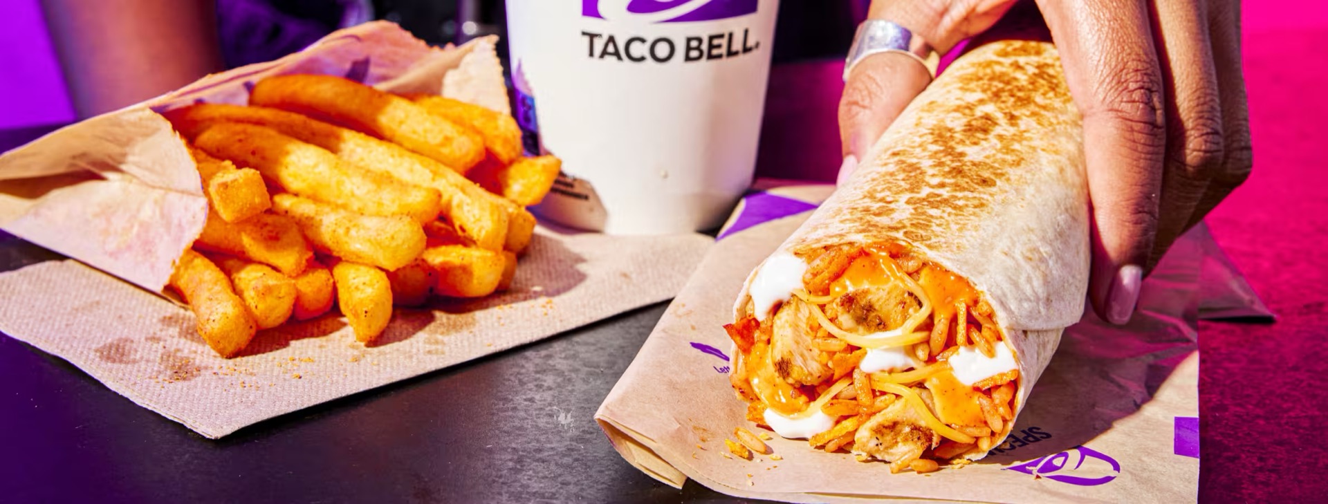 A burrito and fries on a tray under purple light.